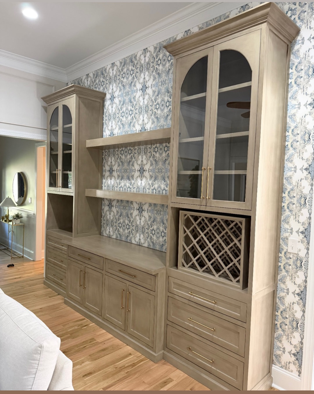 Full view of custom natural wood cabinets with arched glass doors, open shelves and wine storage against blue patterned wallpaper