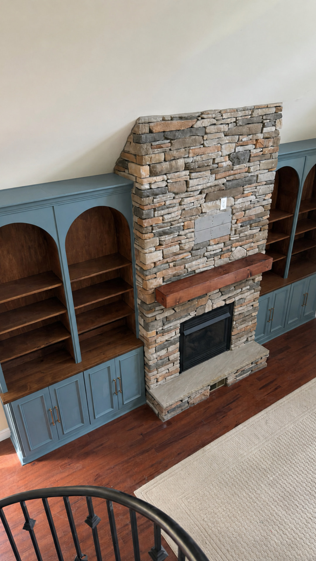 Full room view of custom blue arched bookcases and wood shelves fitted around a tall stone fireplace