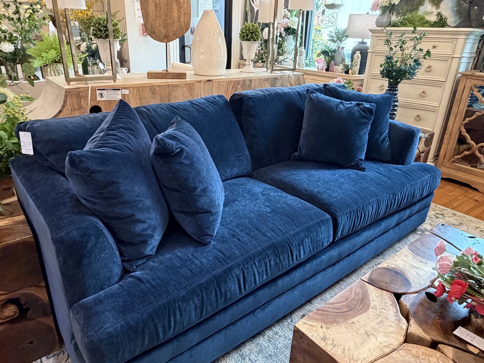 A deep blue velvet sofa styled with a live edge wood coffee table at MONA Boutique
